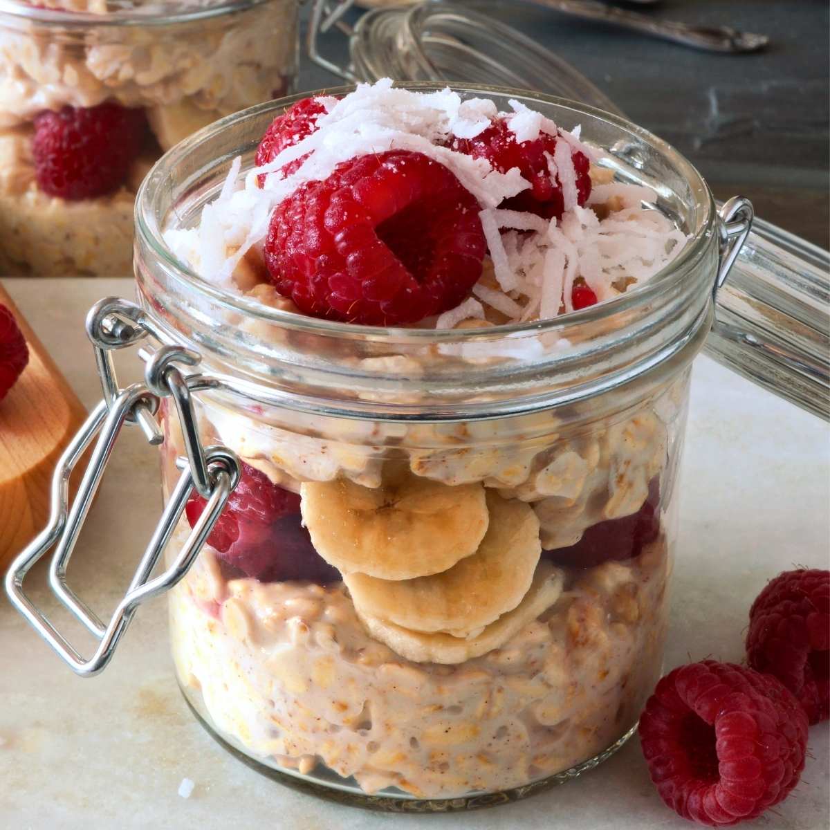 Layered oatmeal breakfast jar with banana, raspberries, and shredded coconut