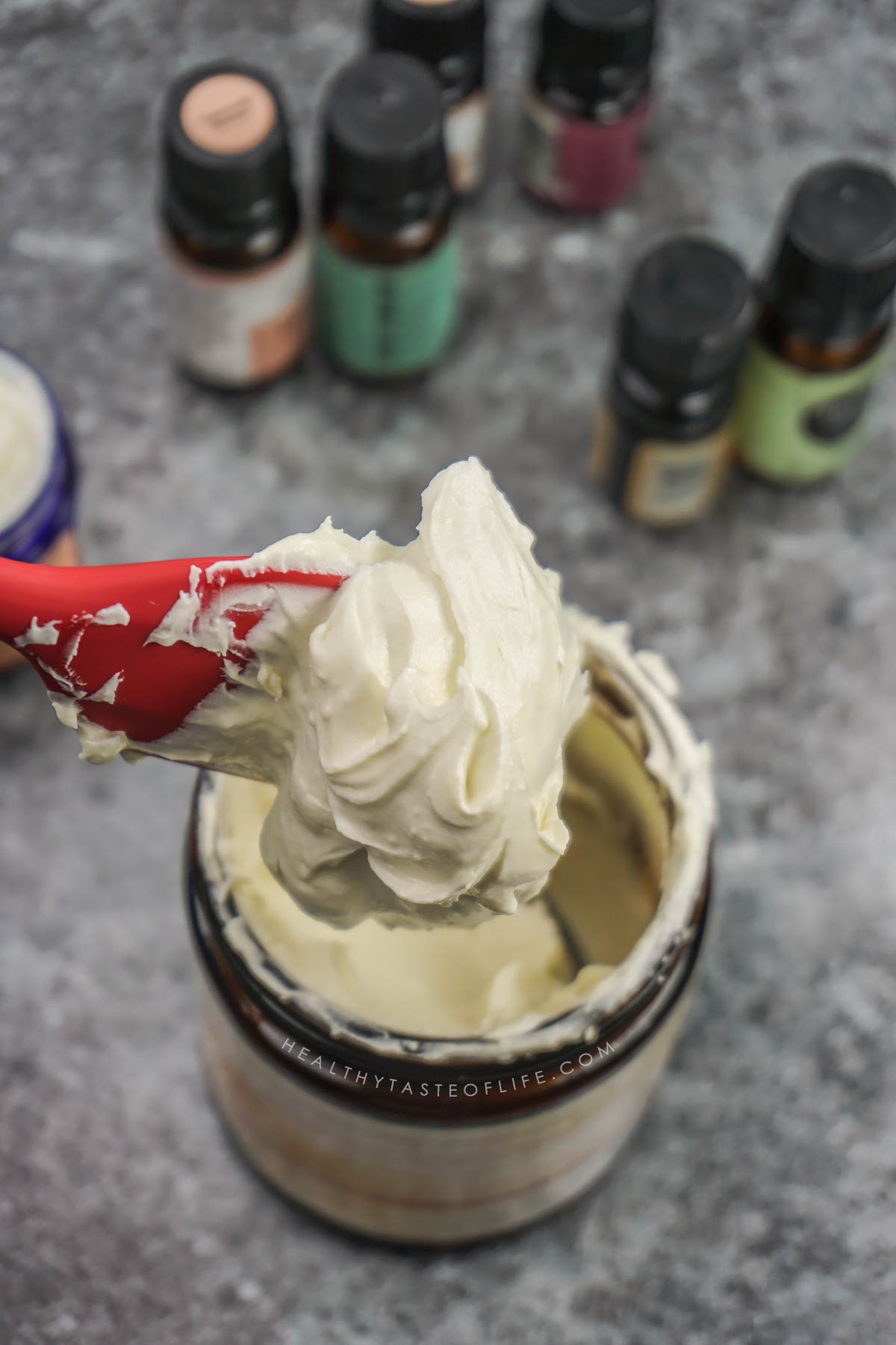 Mango body butter transferred to a storage jar showing creamy whipped texture on a spatula perfect for dry skin and eczema prone skin.