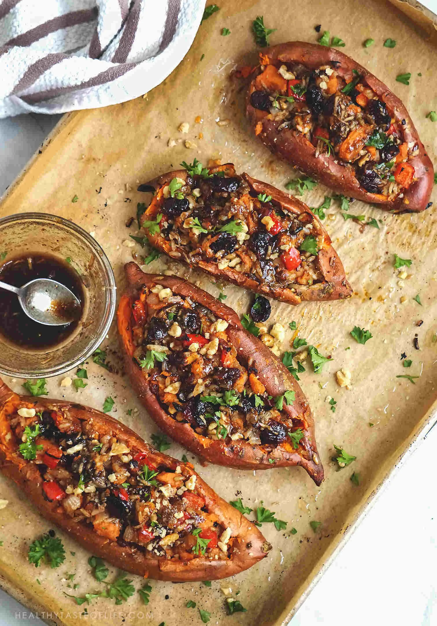 Overhead shot of baked sweet potatoes stuffed with savory filling comprised of rice, veggies, dried fruit and nuts finished with balsamic sauce.