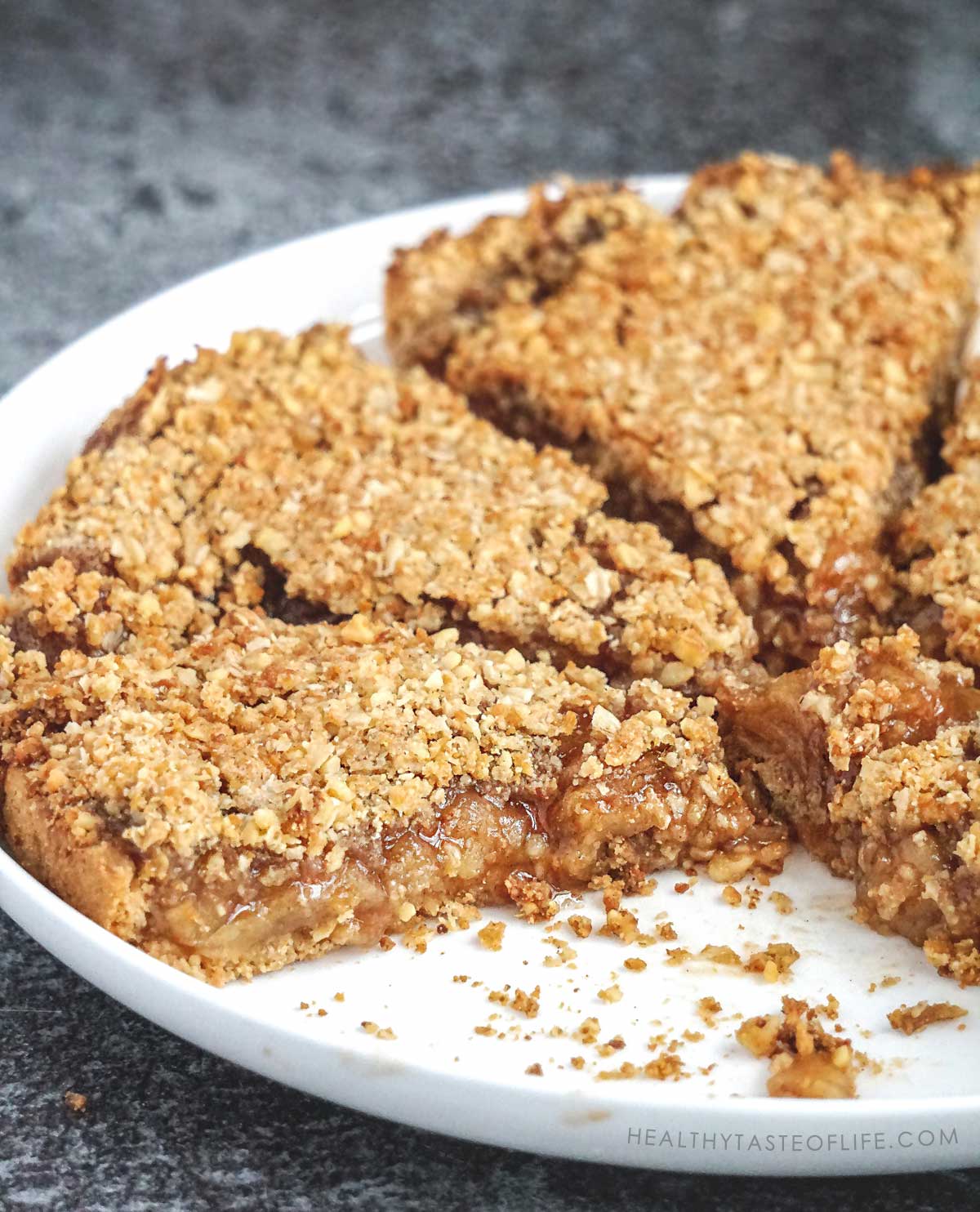 Fresh baked gluten free apple pie with golden oat crumble topping in a round glass pie dish sliced for serving.
