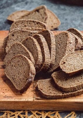 Sliced Pumpernickel-style gluten-free sourdough loaf on a wooden board showing texture.