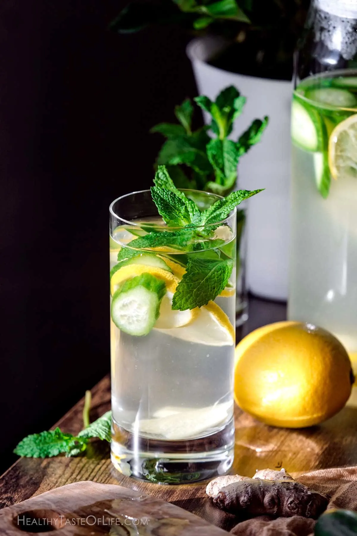 A glass of water infused with lemon ginger and cucumber and garnished with mint leaves.