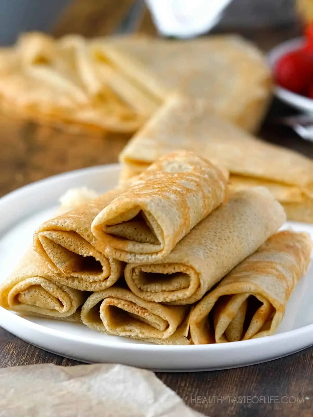 Thin pliable gluten free crepes rolled up on a plate.
