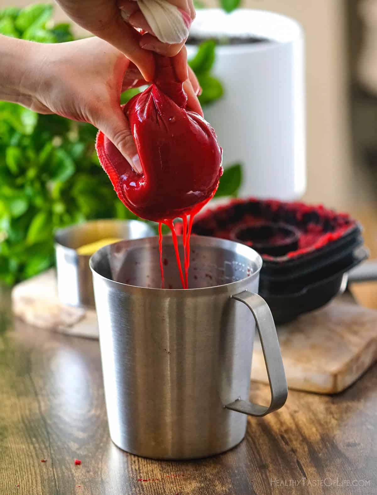 Squeezing beet juice through a nut milk bag into a container.