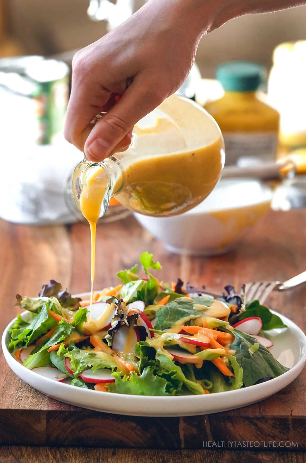 Pouring the mayo free honey mustard sauce over a plate of salad.