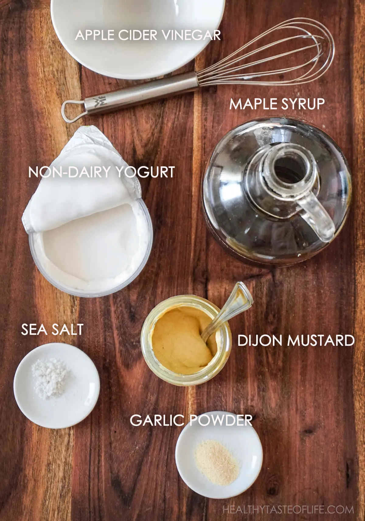 Ingredients for dairy free honey mustard dressing displayed on a board: Dijon mustard, maple syrup, dairy free yogurt, apple cider vinegar garlic powder, sea salt.