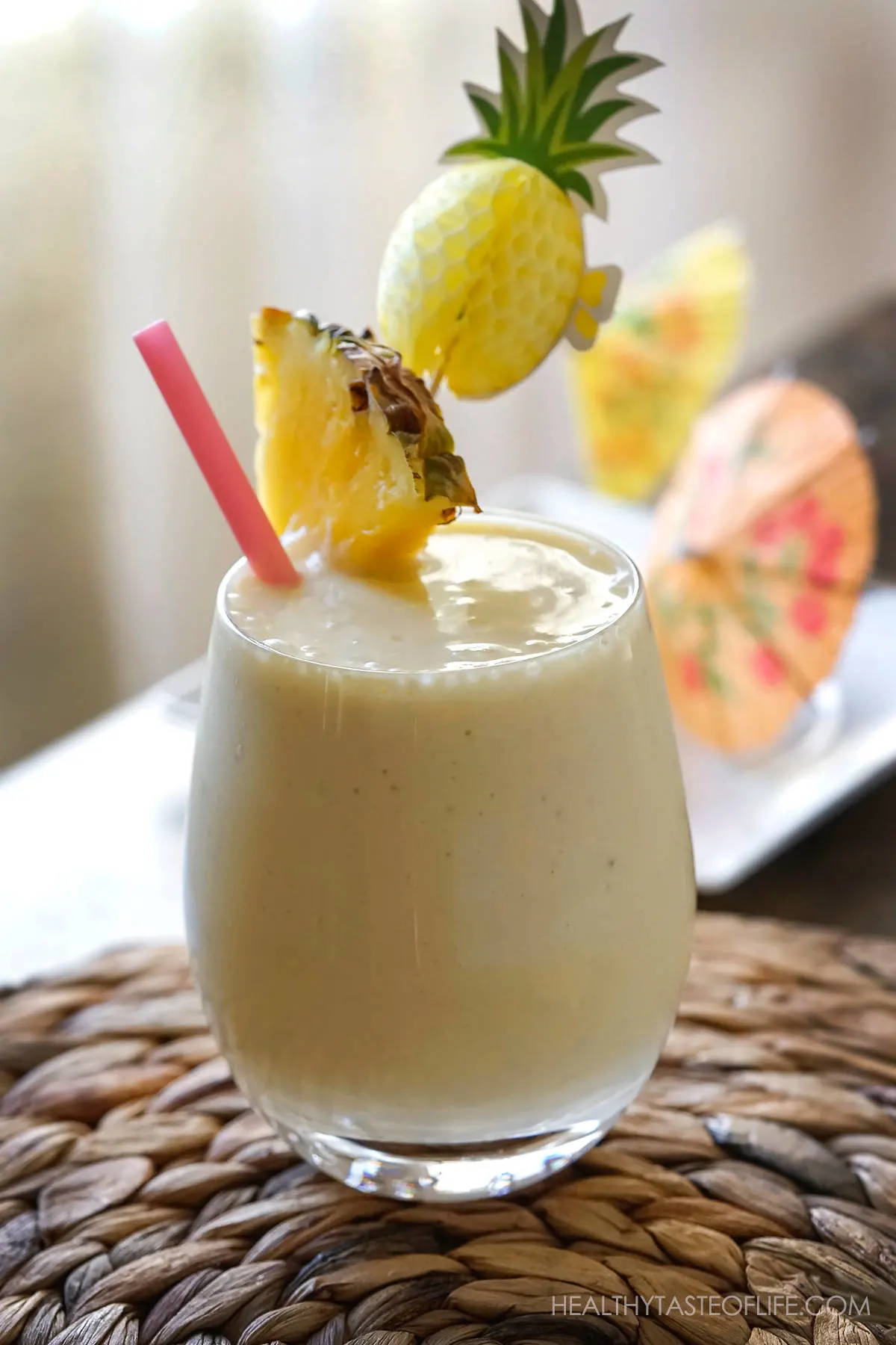 Pineapple milkshake in a glass with pineapple wedge, straw and cocktails umbrella.