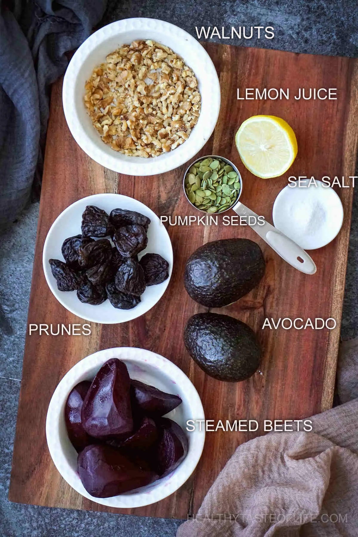 Ingredients for a vegan beet salad displayed on a board: steamed beets, crushed walnuts, avocado, prunes, pumpkin seeds, lemon and salt.