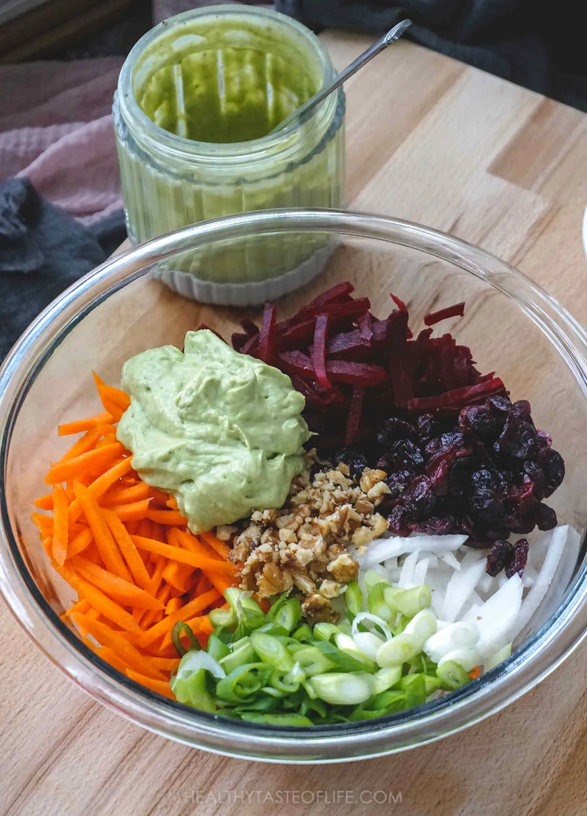 Ingredients for beet salad in a bowl: beetroot, carrots, radish, scallions, walnuts and avocado dressing.