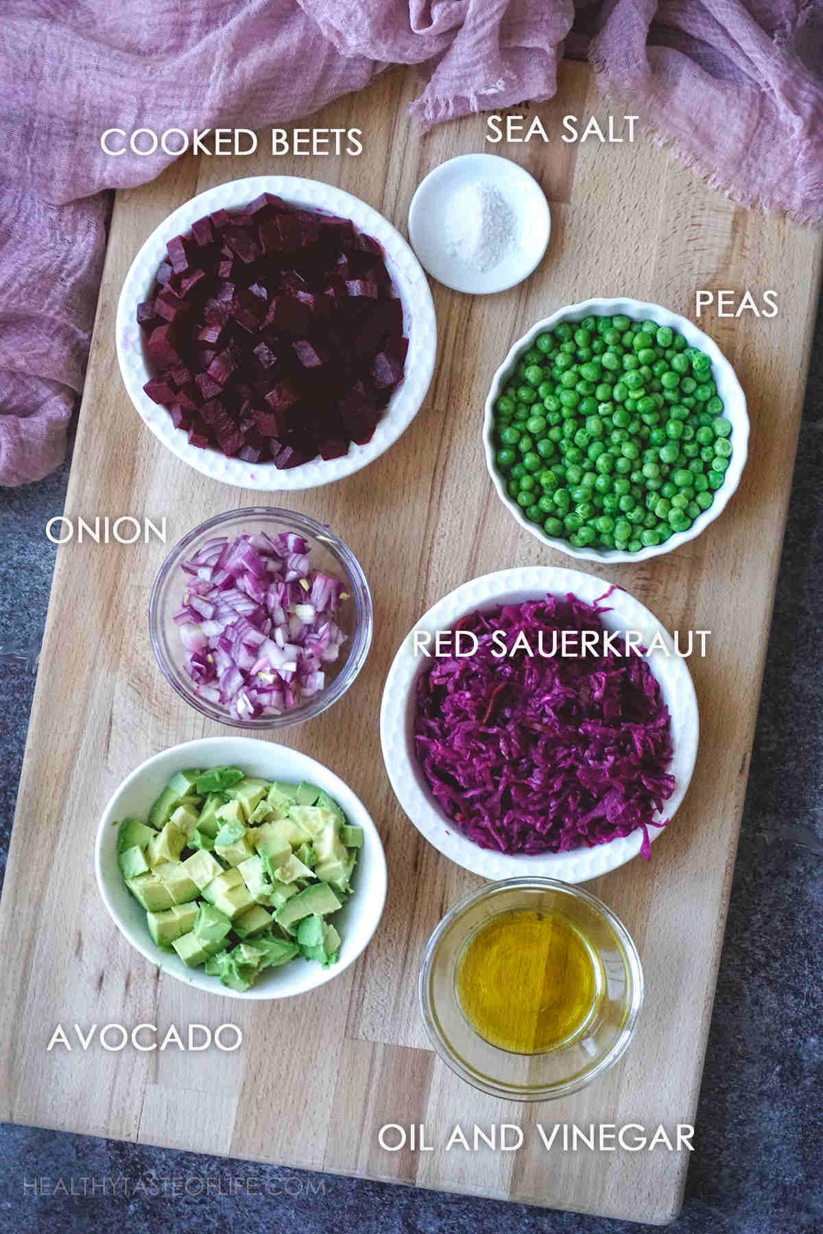 Ingredients for Russian Vinaigrette displayed on a board: roasted beets, peas, sauerkraut, onion, avocado, salt, vinegar.