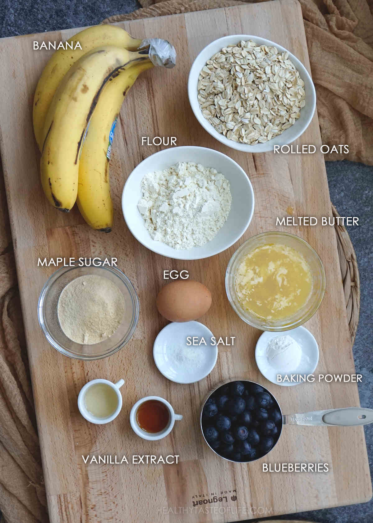 Ingredients for making oatmeal banana blueberry muffins displayed on a board.