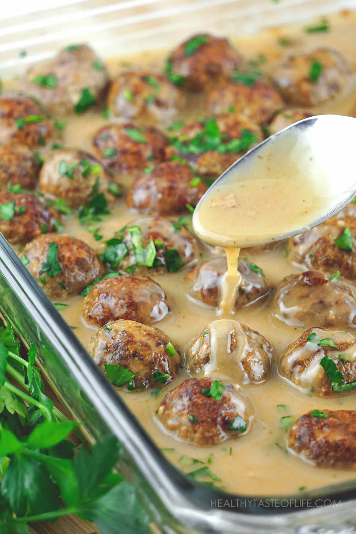 Gluten free Swedish meatballs with ground beef and ground turkey cooked with dairy free gravy in a baking dish and garnished with chopped parsley.