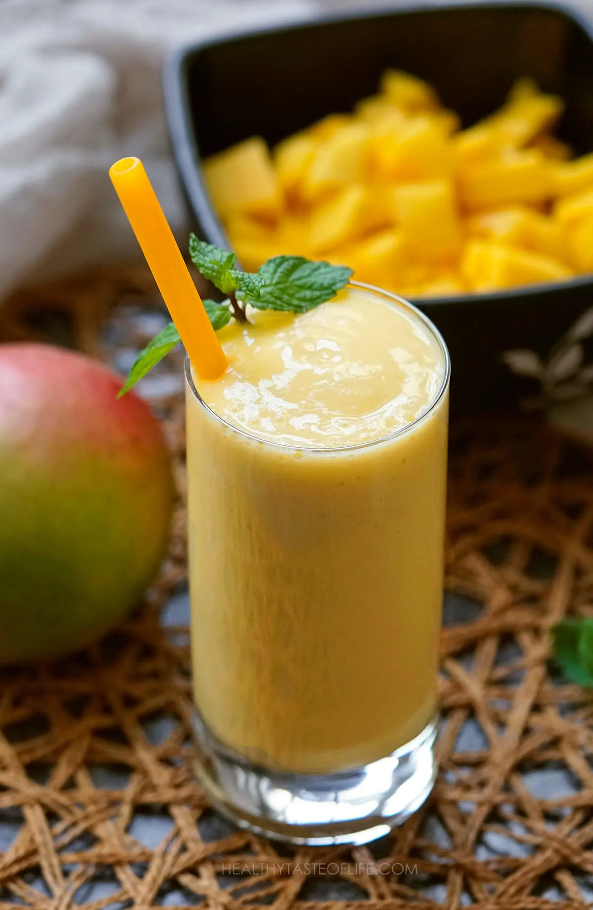 Pineapple mango smoothie in a tall glass garnished with mint leaves.