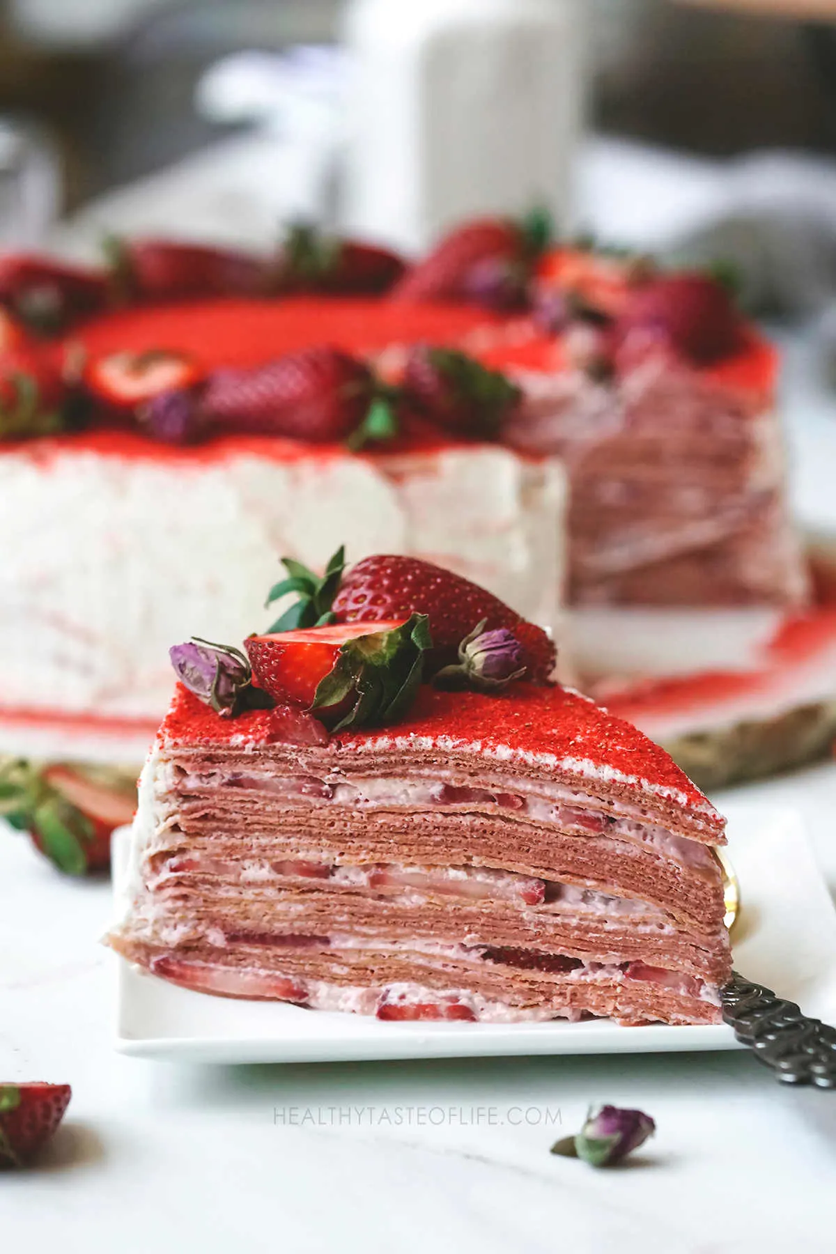 A slice of strawberry crepe cake with fresh strawberries between layers.