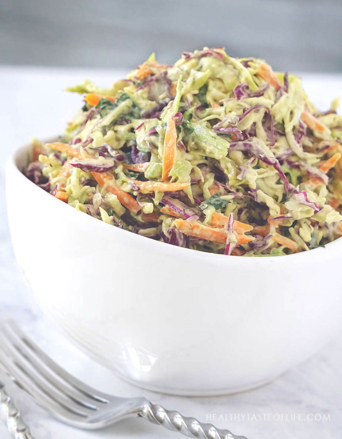 Healthy avocado coleslaw with purple and green cabbage in a bowl.