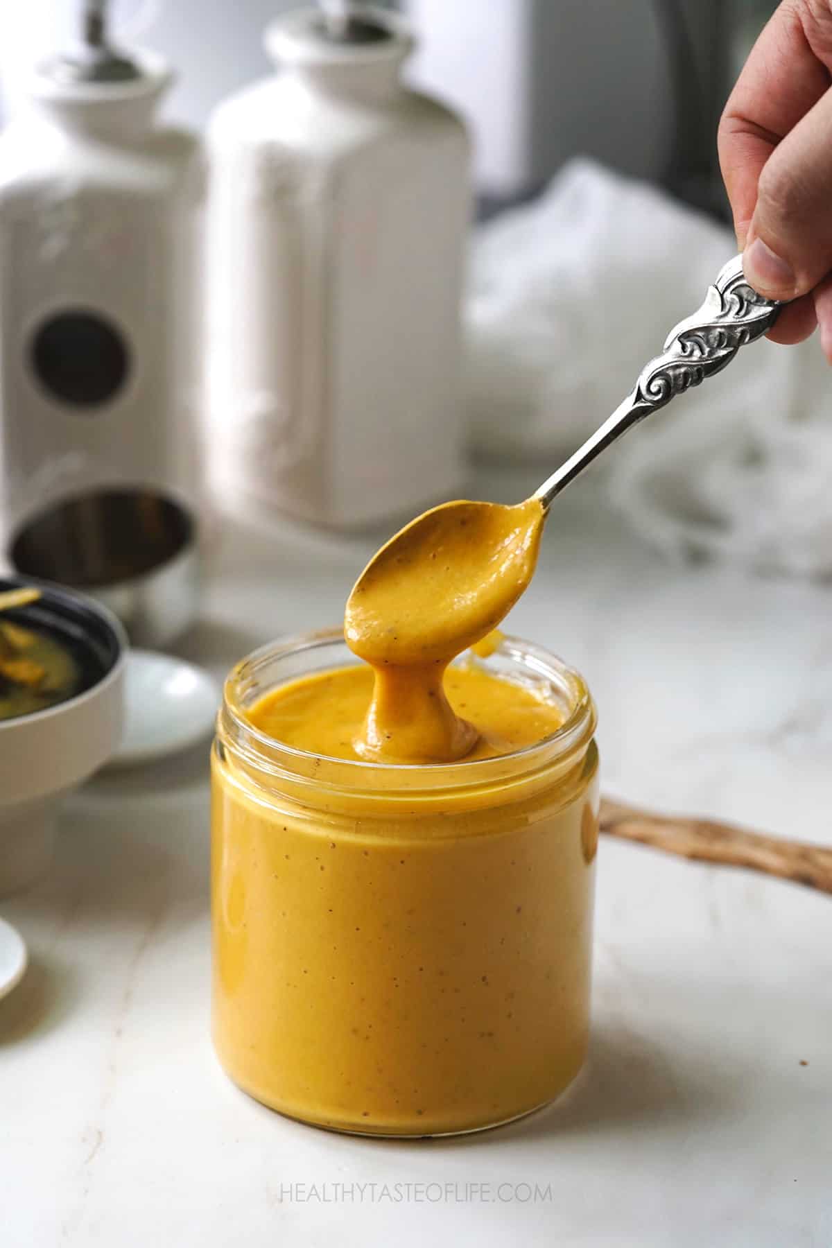 Mango sauce in a jar showing creaminess of texture with a dipping spoon.