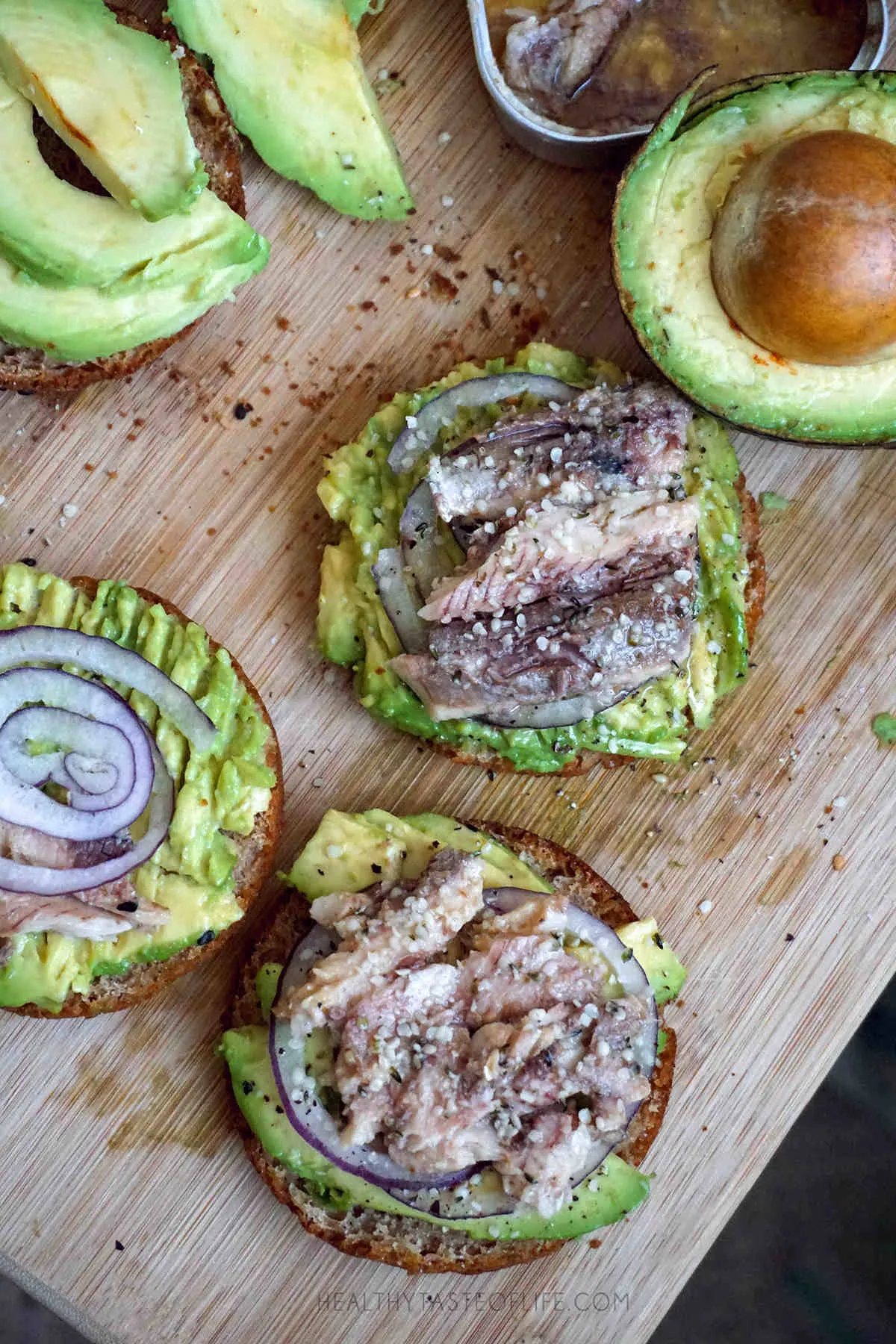 Gluten free dairy free avocado toast made with homemade gluten free buns topped with sardines, red onion and finished with hemp seeds.