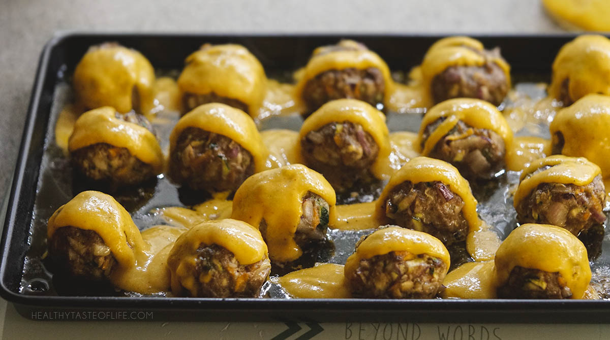 Baked beef meatballs taken right out of the oven and the mango sauce being poured immediately.