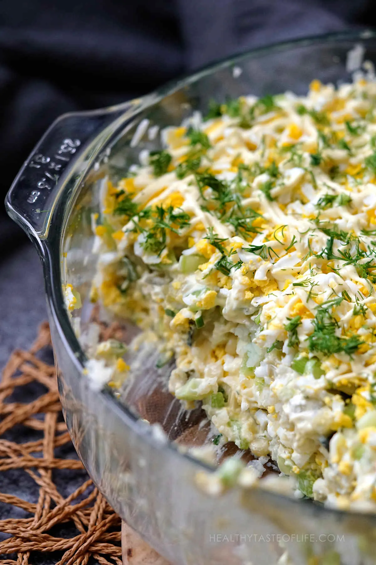 close up shot of potato & egg salad served in a glass dish for Easter, one partion removed showing inside layers ans structure.