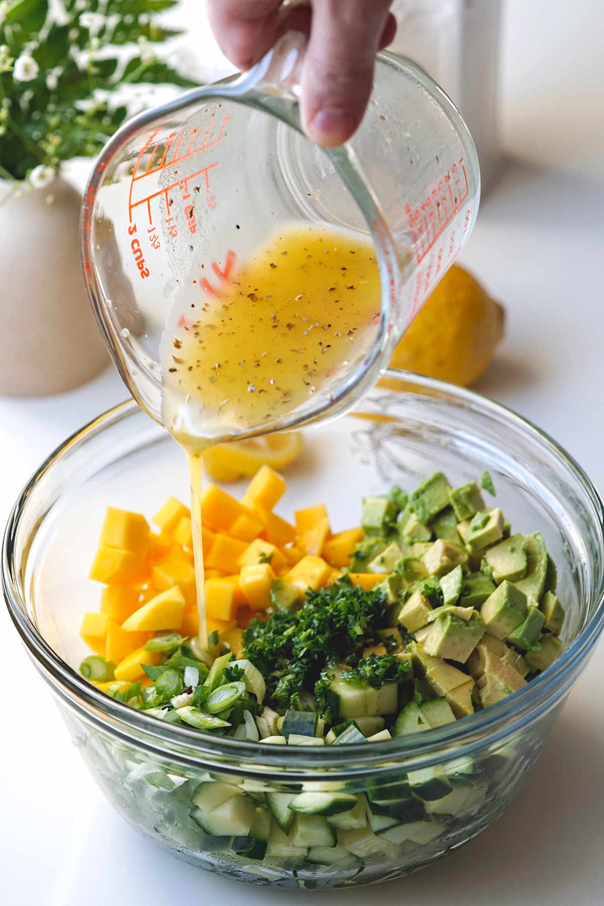 Shot showing how the dressing is poured over the mango cucumber avocado salad before it's mixed.