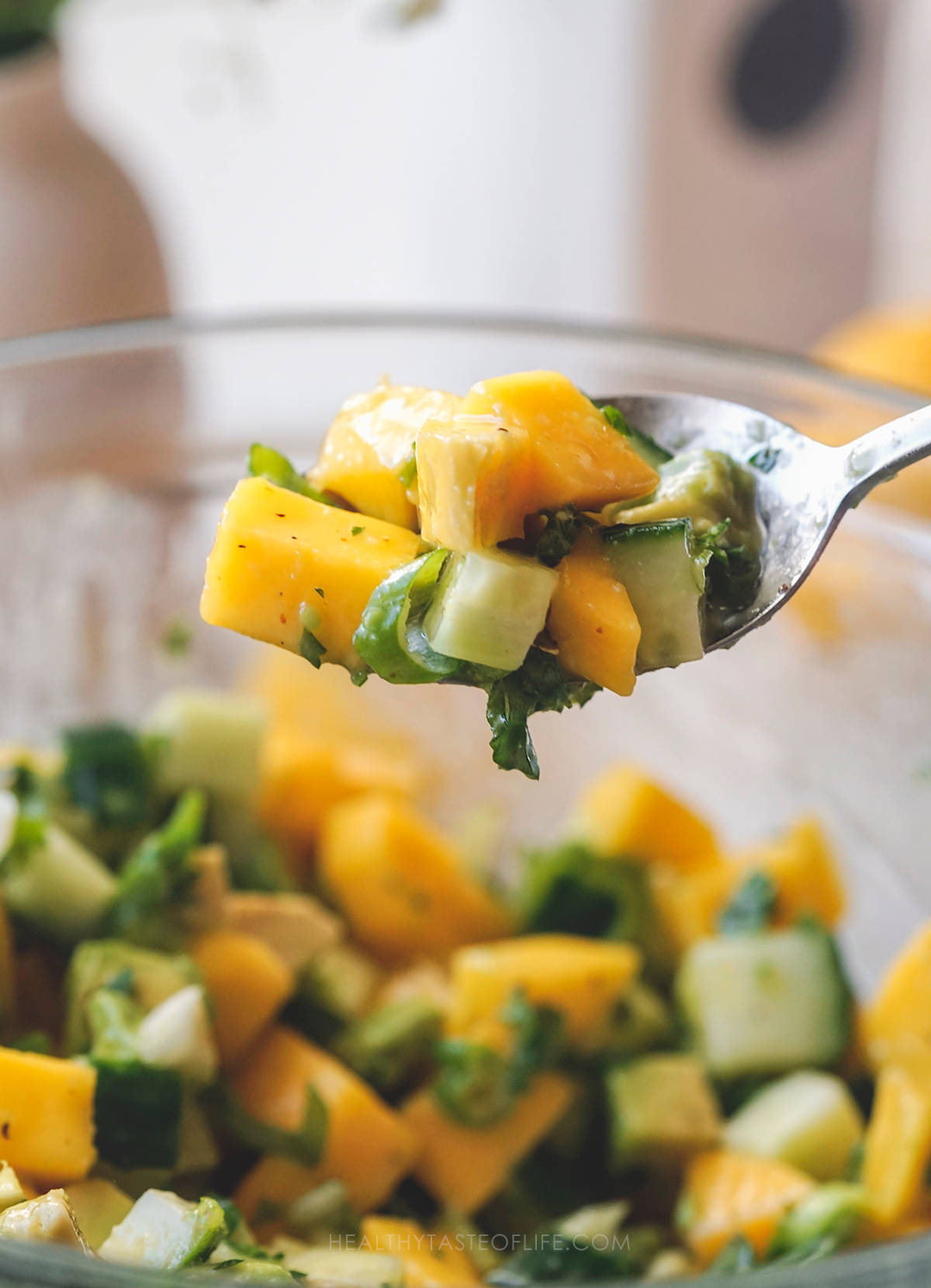 Close up shot: spoonfool of mango cucumber salad with cubed avocado and mixed with dressing.