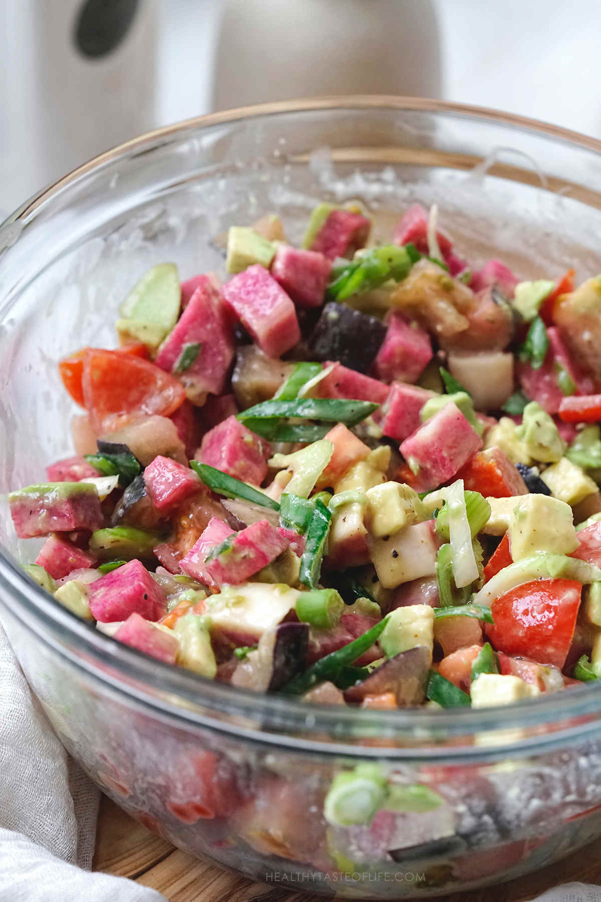 Assembled salad with watermelon radishes avocado tomatoes and spring onions in a bowl.