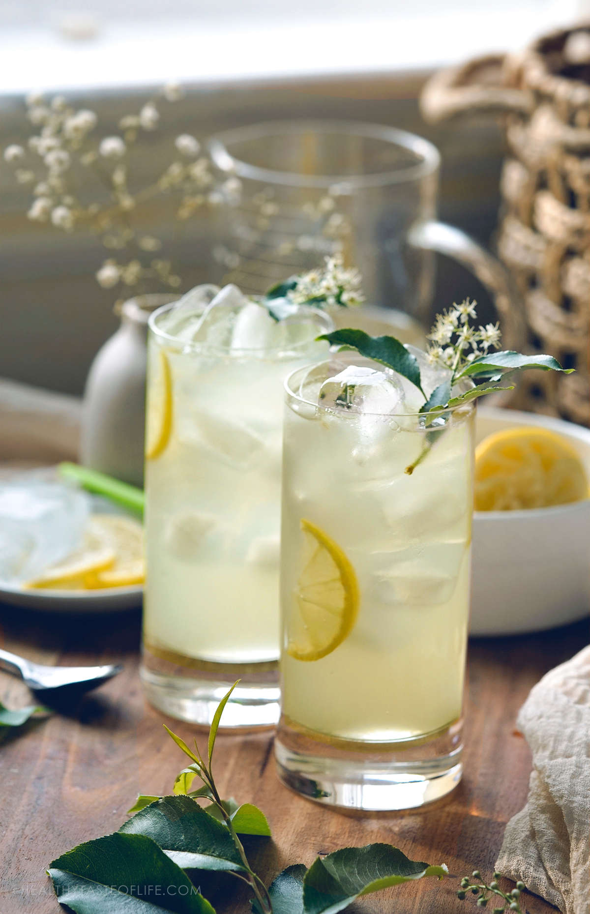 Close up shot of elderflower lemonade with ice and garnished with lemon and elderflower leaves.