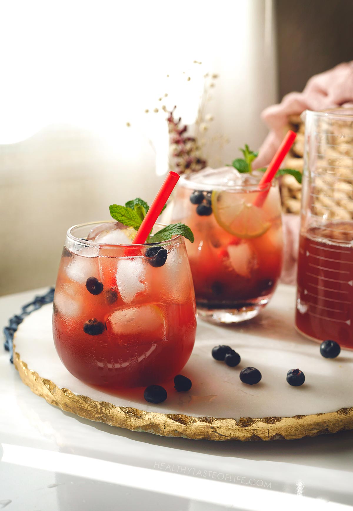 Elderberry lemonade served in two glasses over ice, decorated with lemon slices and berries and a mint sprig.