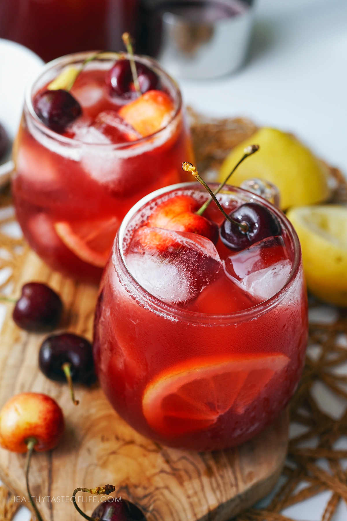 Cherry lemonade served in glasses over ice, garnished with fresh cherries and a slice of lemon.