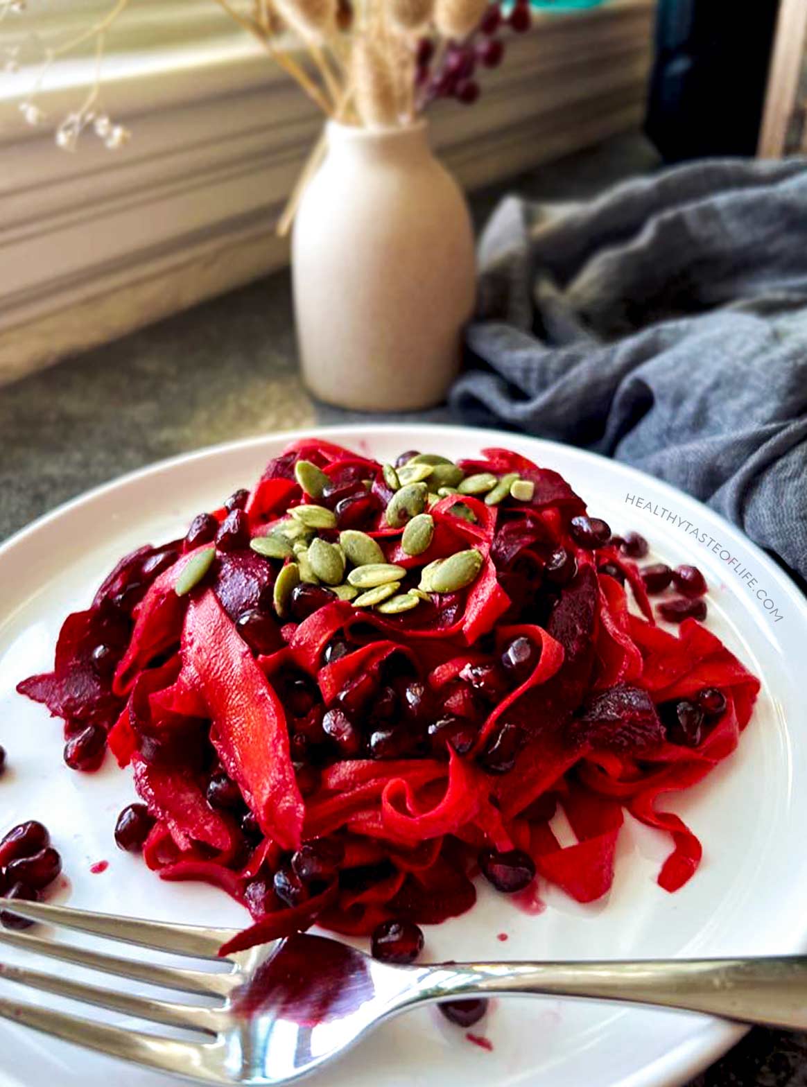 Colorful healthy beet pomegranate salad with tahini citrus dressing served on a plate with pumpkin seeds.