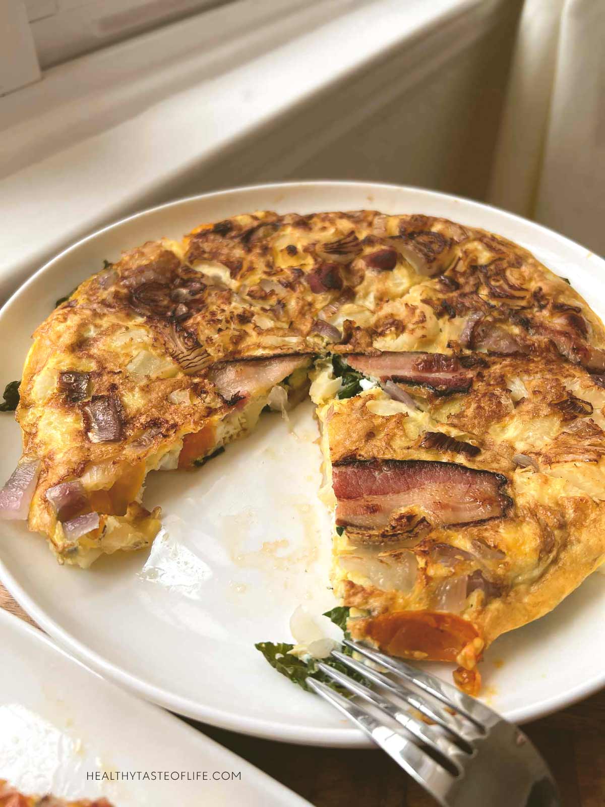 Veggie omelette with cauliflower and bacon sliced and a wedge taken out.