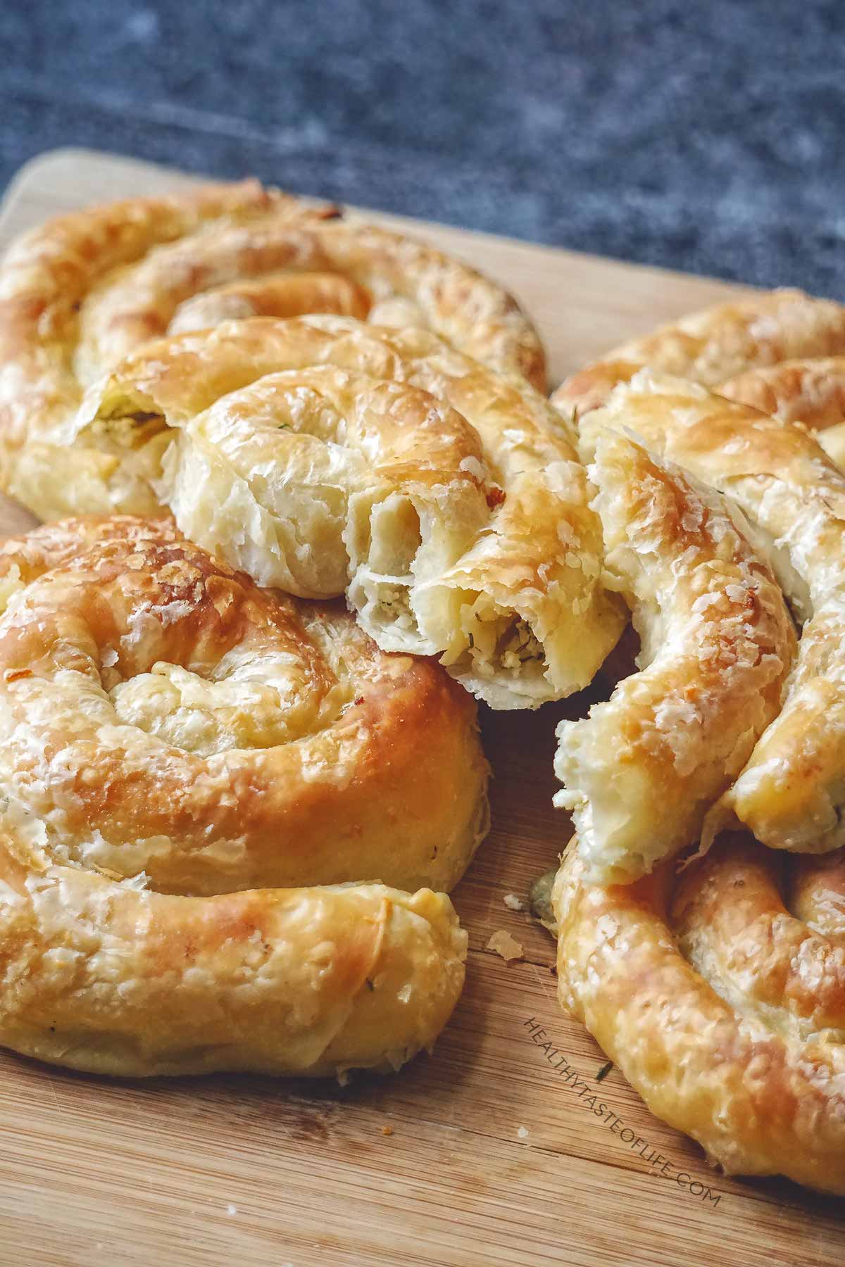 Baked savory cheese puff pastry pinwheels (spirals) - flaky layers - showing texture inside resting on a board.
