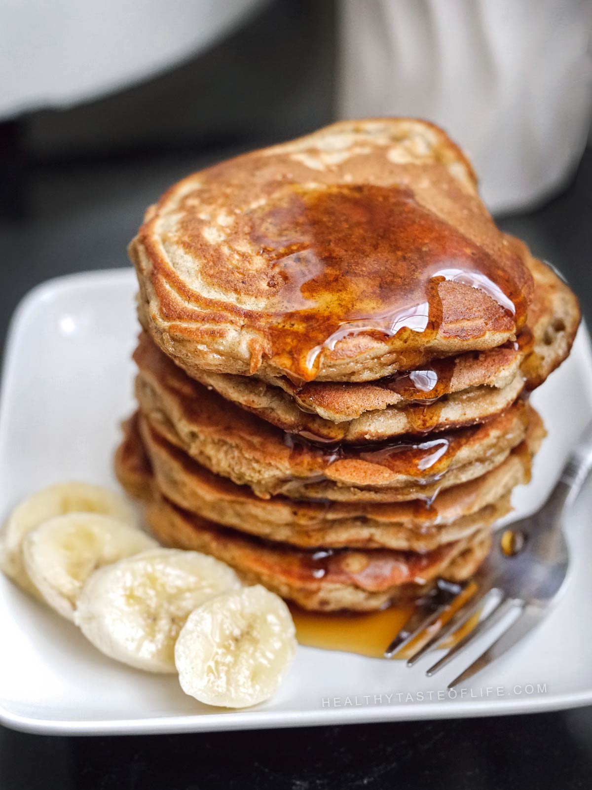 Stack of soft gluten free banana pancakes (dairy free) garnished with slices of fresh banana and drizzled with maple syrup.